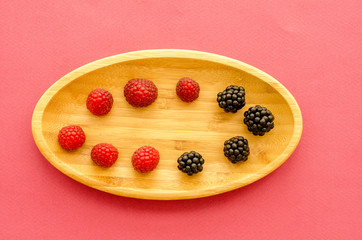 wooden plate with berries on a pink background