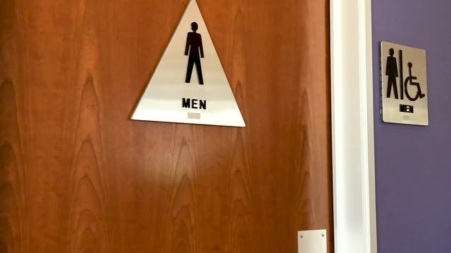 Men's restroom sign on wooden door in office environment.