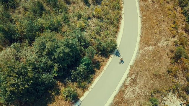 Aerial View cyclist rides on the road on summer sunny day light in the trees and mountains outdoors background, Drone 4K Video