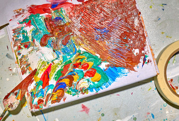 Palette and palette knife covered by colorful paint on the white table