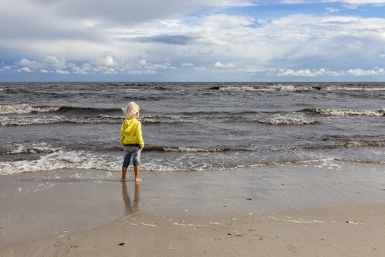 A little boy stands on the shore of a windy sea.