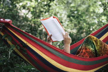 Young woman reading a book lying in a hammock