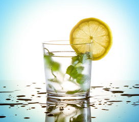 Cold drink: lemon, mint and ice cubes. Spilled water and reflection.