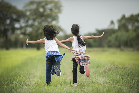 Two little cute girls are running on green grass. Best friends.