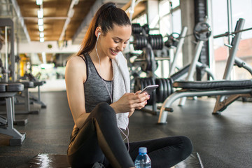 Fototapeta na wymiar Attractive fit woman using phone after sports training in gym