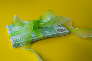 pack of hundred euro banknotes with green bow-knot on yellow desk, gift or dividends concept, european union money