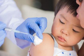 Doctor giving an injection vaccine to a girl. Little girl crying with her mother on background.