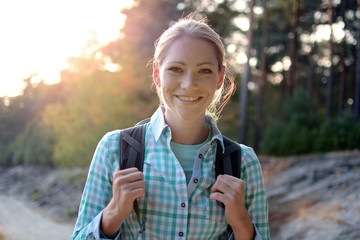 Young woman with backpack hiking through forest and nature on a sunny summer day