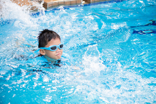 Soft focus on Happy young asian kid with swim goggles swimming in pool.