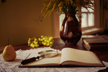 Old books on a wooden table and glass magnifier.Cute composition with old books in shabby grey cover and bouquet of flowers in a cup on wooden background. Vintage objects. Romantic decor elements
