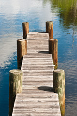Fototapeta premium Top view, medium distance of a vintage, wood dock, walkway, supported by six wood pilings in the water of a tropical creek, on a summer, sunny late afternoon
