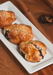 top view, close up of a white, retangular plate with three, freshly baked, homemade, golden,  blueberry scones on a wood serving board