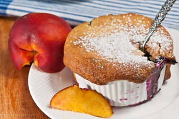 top view, close up of a white ramekin , filled with freshly baked, homemade blueberry, peach cobbler wi section of ripe peach on white, round plate