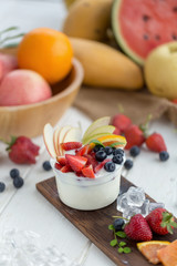 Healthy fruit salad with yoghurt on a wooden plate with ice cubes and fruit as background