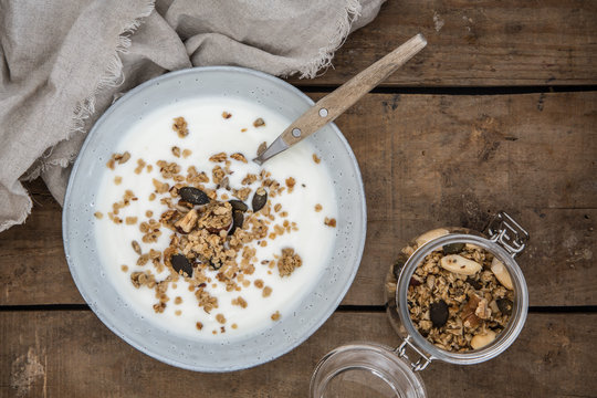 Sch&uuml;ssel mit Joghurt und Granola aus Haferflocken, N&uuml;ssen, Leinsamen, Sonnenblumenkernen und K&uuml;rbiskernen auf einem alten Holzuntergrund