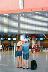 People Travel In Airport. Couple Looking At Flight Board