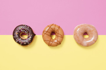 Three donuts (doughnuts) on a split pink and yellow background