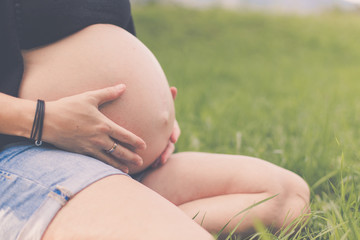 Schwangere junge Frau mit Babybauch sitzt draußen in grüner Wiese
