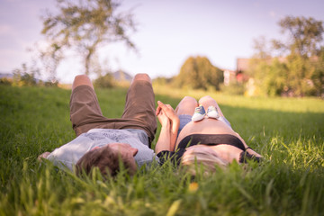 Schwangere junge Frau und ihr Partner liegen draußen im Gras, Unschärfe