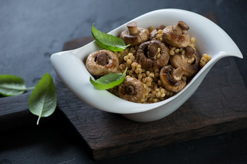 White bowl of pasta with fried mushrooms on a black wooden serving board, studio shot