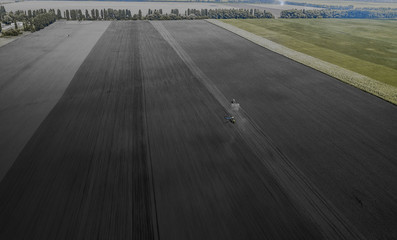 Aerial view of two blue tractors plows the earth in field on a summer day against a black earth...