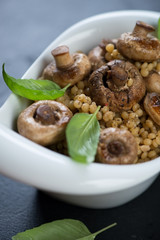 Closeup of pasta served with roasted champignons and ceps in a white bowl, selective focus, vertical shot
