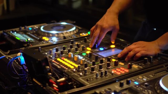Man DJ playing with mixer and digital turntables. CDJ turntables with wires, button and sliders being played by electronic music Disc Jockey at nightclub.