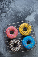 Fototapeta na wymiar Four different donuts on a metal cooling rack, view from above with copyspace, grey concrete surface