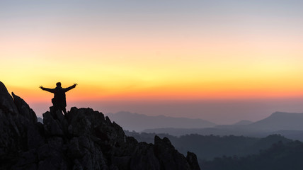 silhouette of a standing man on top of a cliff mountain with arms raised during sunset celebrate success - landscape sunset Thailand