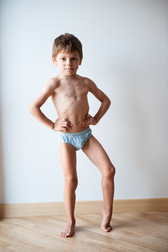 strong healthy little caucasian boy in shorts showing his body muscle indoors