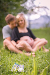 Schwangere junge Frau und ihr Partner sitzen draußen im Gras, Unschärfe