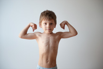 strong healthy small caucasian kid showing biceps muscle indoors