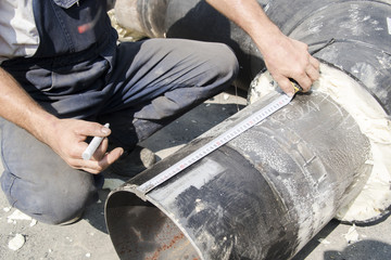 The worker measures and marks something on the pipes, photographed on the building