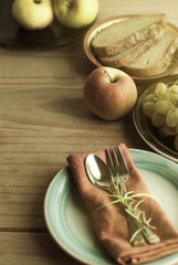 Fork and spoon over napkin, with a twig of rosemary. Fruits and bread on background. Healthy food. Rustic wooden background. Food education.