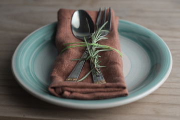 Fork and spoon over napkin, with a twig of rosemary. Rustic wooden background. Food education. Healthy food. Copy space.