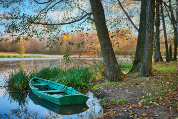 Naklejka na ściany i meble Green abandoned boat in the lake in a beautiful autumn park in the early morning