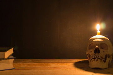 Human skull with candle light and the book on wooden table in the dark background, Decorate for...