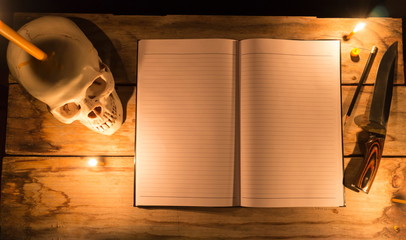 Human skull with candle light and notebook with pencil and knife on wooden table, Decorated for...