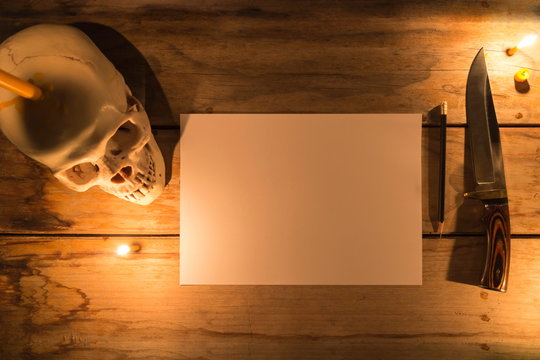 Human skull with candle light and white paper with pencil and knife on wooden table, Decorated for Halloween Theme with copy space.