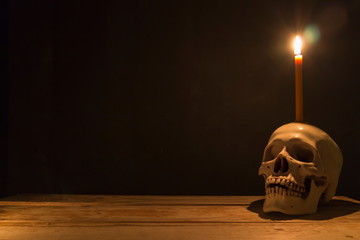 Human skull with candle light on wooden table in the dark background, Decorate for Halloween Theme with copy space.