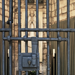 Sculpture of praying clergyman behind locked iron gate and bars.