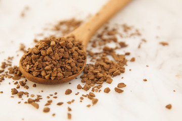 Pile of instant coffee grains in wooden spoon, over marbble surface. Caffiene drink. Copy space.