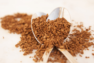 Pile of instant coffee grains in metal spoons, over marbble surface. Caffiene drink.