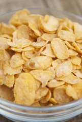 bowl of sugar-coated corn flakes and spoon for breakfast or snack over rustic wooden background.