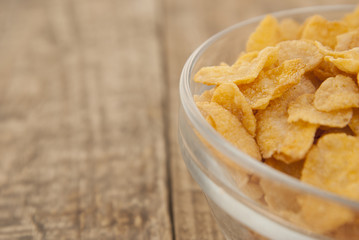 bowl of sugar-coated corn flakes and spoon for breakfast or snack over rustic wooden background.
