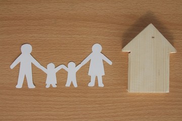 Family cut out paper with mini wood house model on wood background.