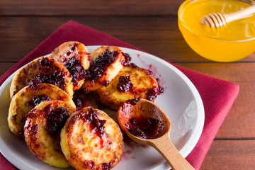 Cottage cheese pancakes on a wooden background. Traditional Ukrainian dish - syrniki with jam on a red napkin. Pancakes with cottage cheese on a white plate with honey and rowan berries
