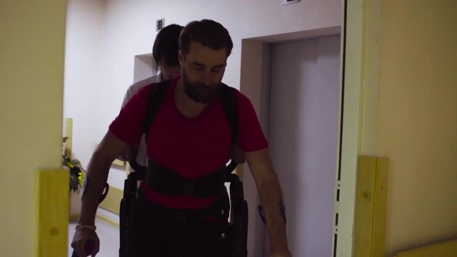 Young disable man walks in the robotic exoskeleton in the rehabilitation clinic. Doctor supports him