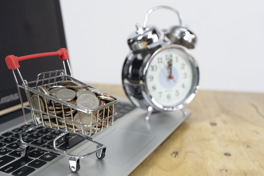 Coin in a trolley on a laptop keyboard and alarm clock. Ideas about online shopping