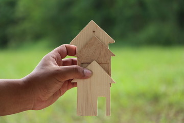 Hand holding Wood house model on nature background,Choosing the right real estate property, or new home in a housing development or community